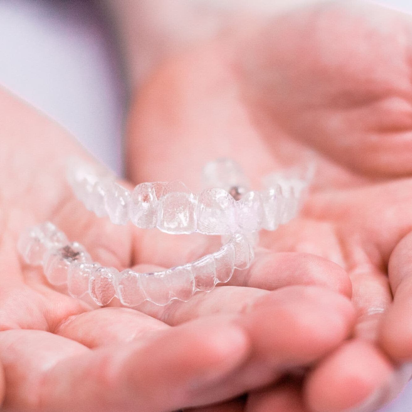 Hands holding a set of Invisalign clear aligners at Luv Braces
